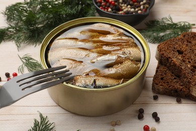 Photo of Tasty sprats in tin can, dill, bread and peppercorns on wooden table, closeup