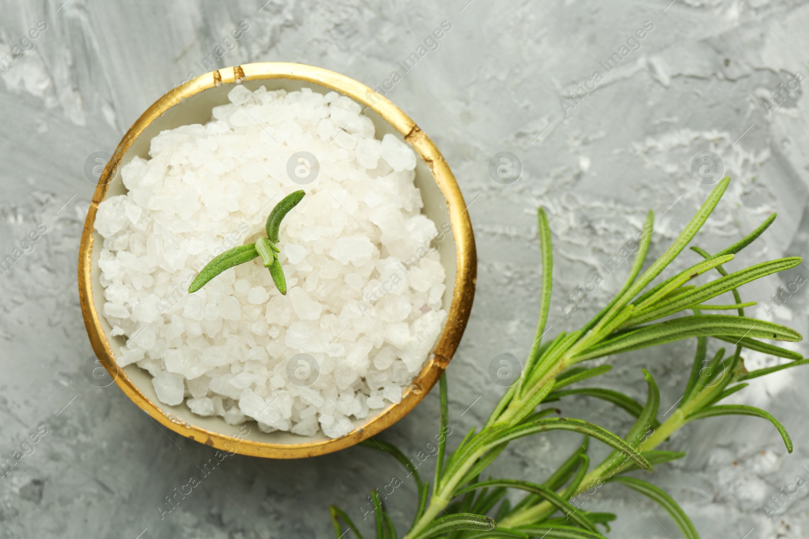 Photo of Sea salt and rosemary in bowl on gray textured table, flat lay