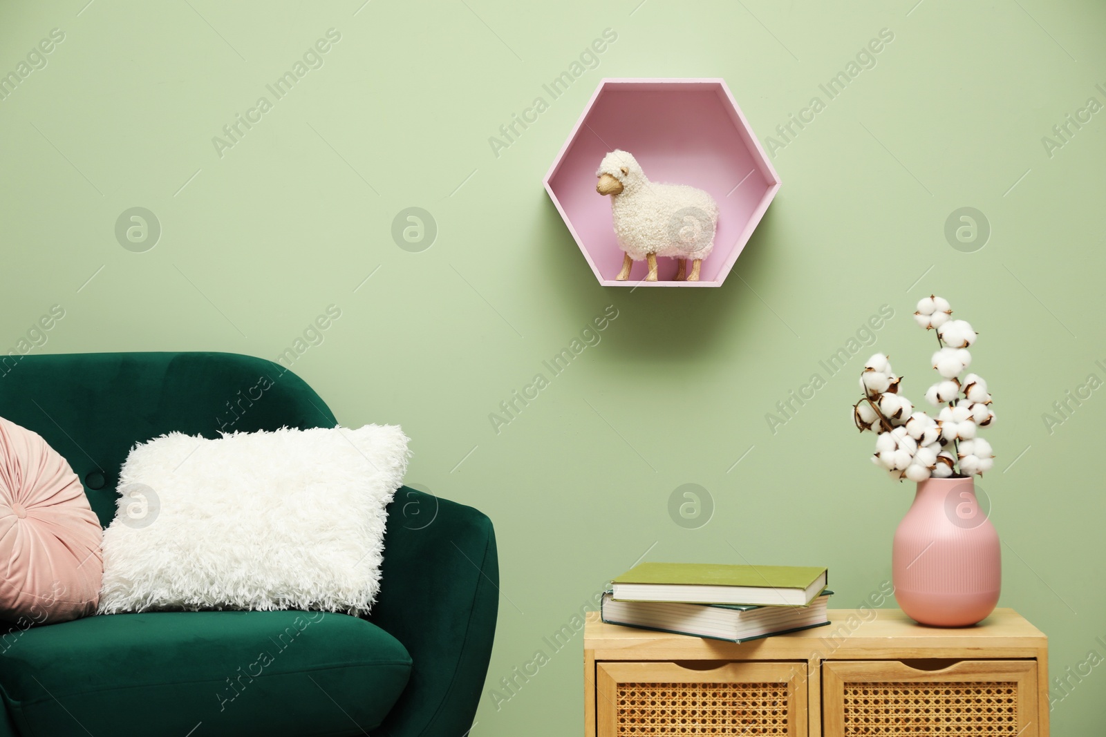 Photo of Stylish green armchair with soft pillows, cotton flowers in vase and books on side table near olive wall