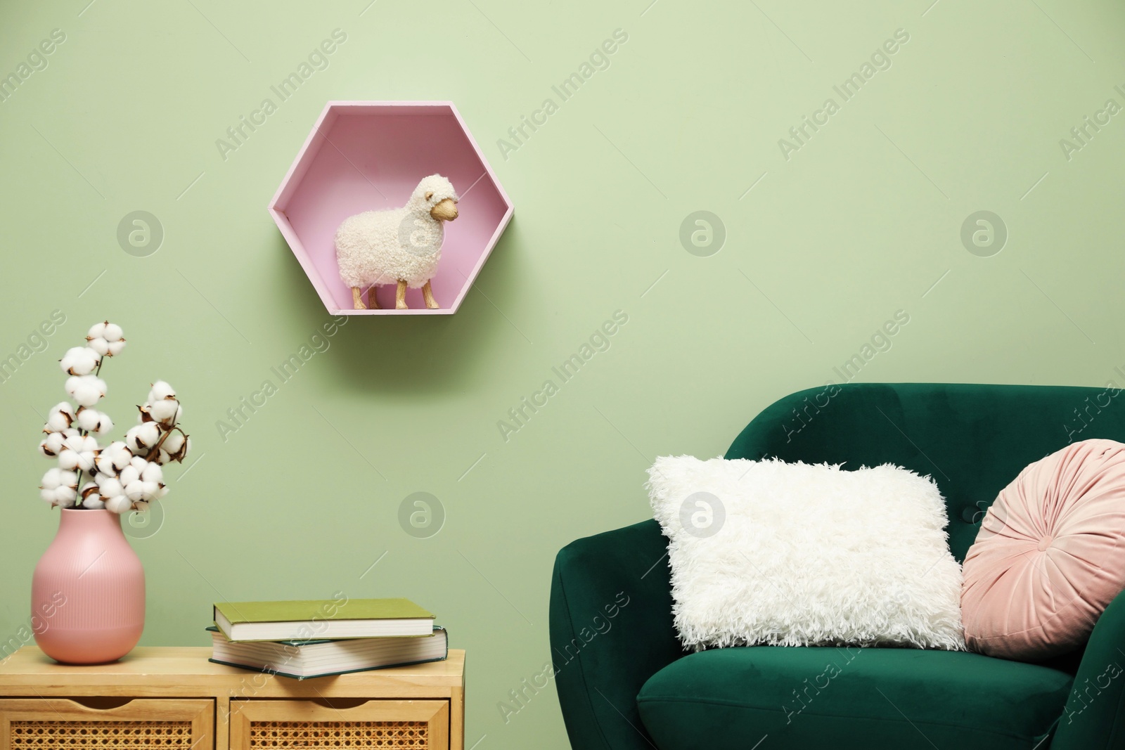 Photo of Stylish green armchair with soft pillows, cotton flowers in vase and books on side table near olive wall