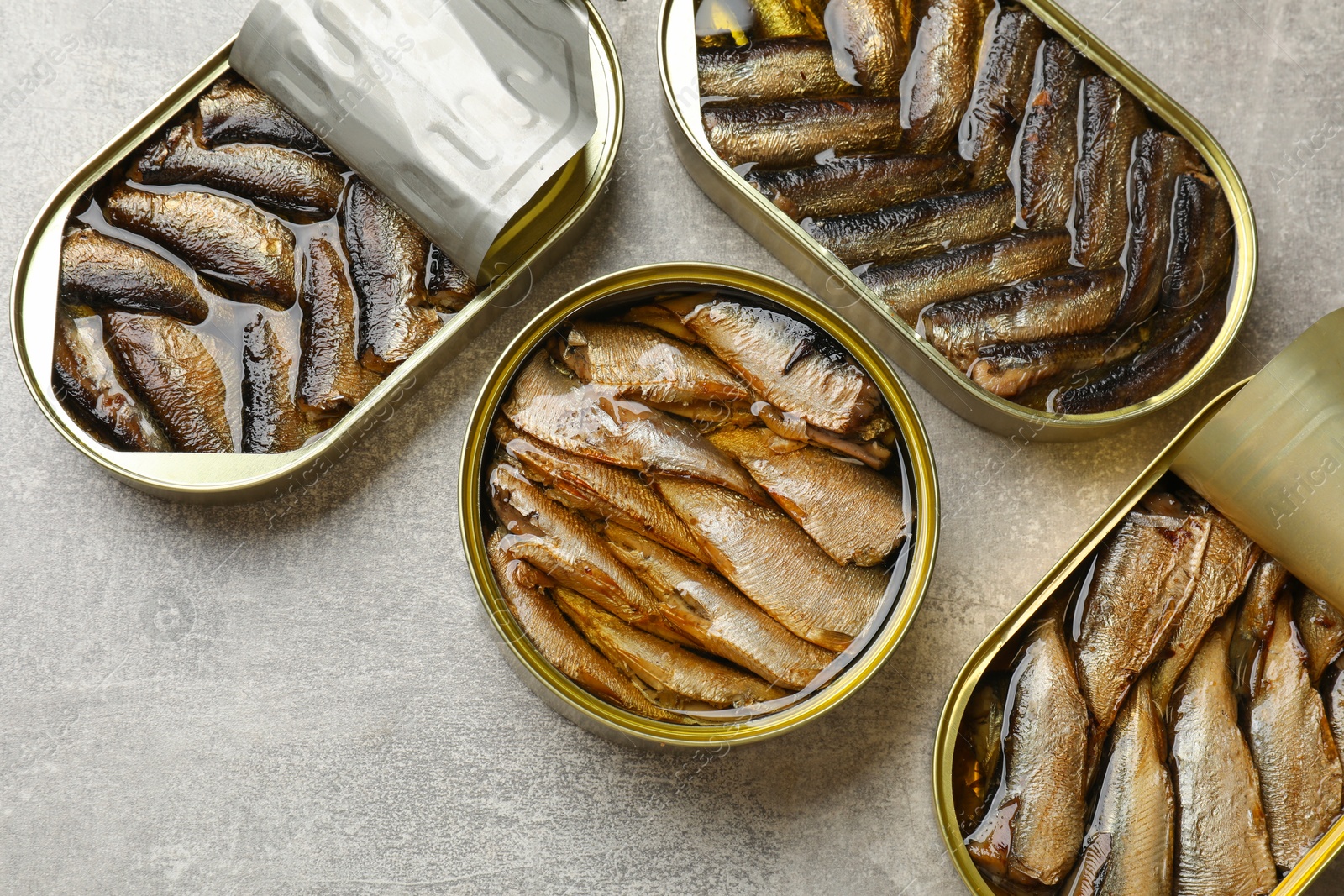 Photo of Tasty sprats in tin cans on grey textured table, flat lay