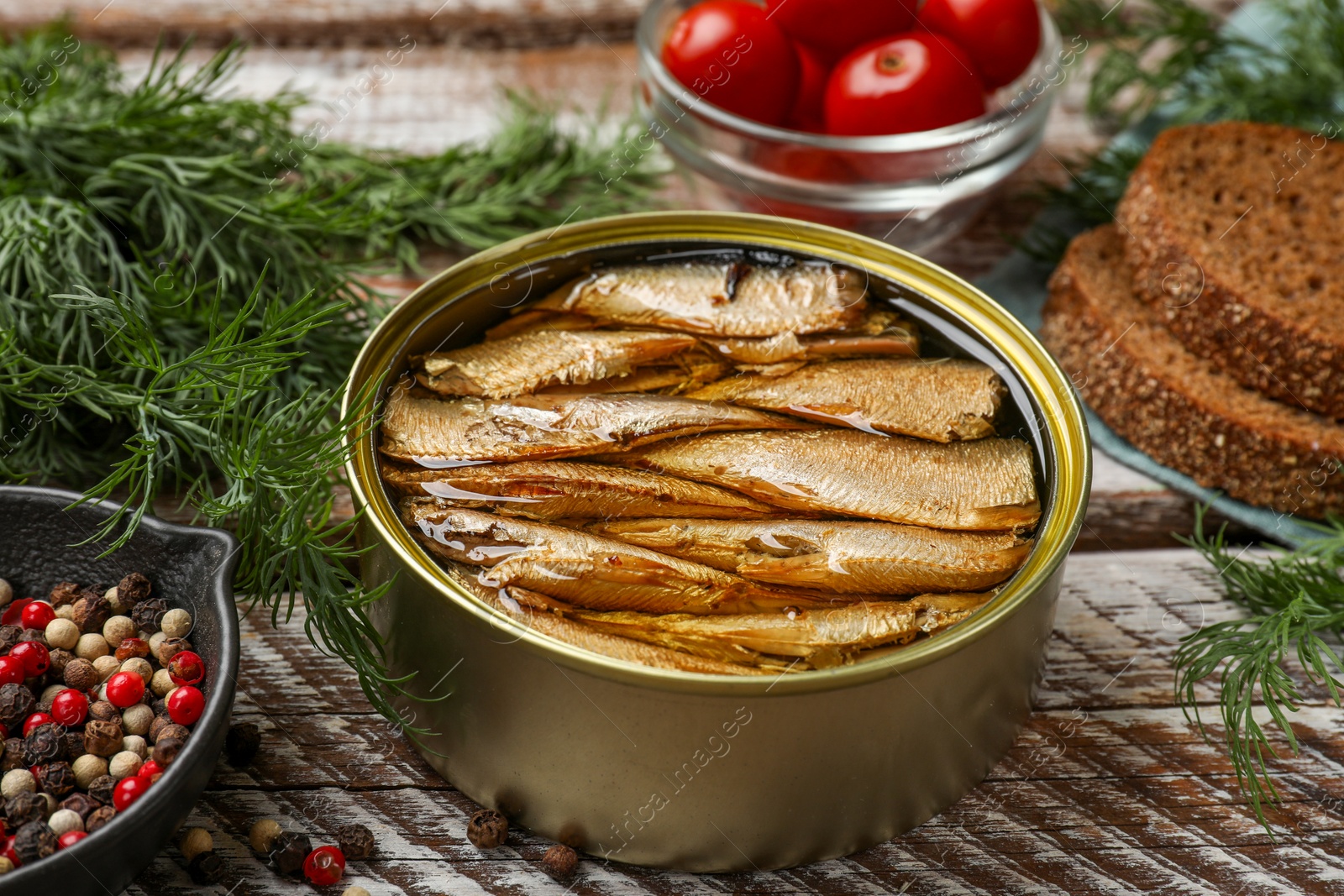 Photo of Tasty sprats in tin can served on wooden table, closeup