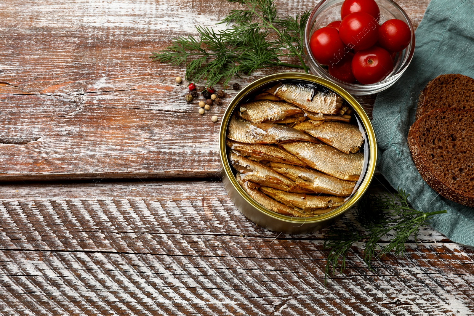 Photo of Tasty sprats in tin can served on wooden table, flat lay. Space for text