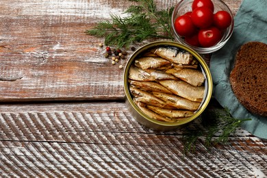 Photo of Tasty sprats in tin can served on wooden table, flat lay. Space for text