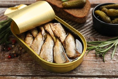 Photo of Tasty sprats in tin can served on wooden table, closeup