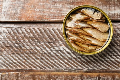 Photo of Tasty sprats in tin can on wooden table, top view. Space for text