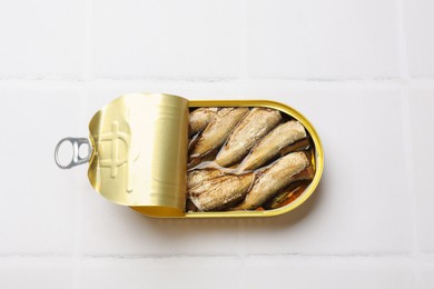 Photo of Tasty sprats in tin can on white tiled table, top view