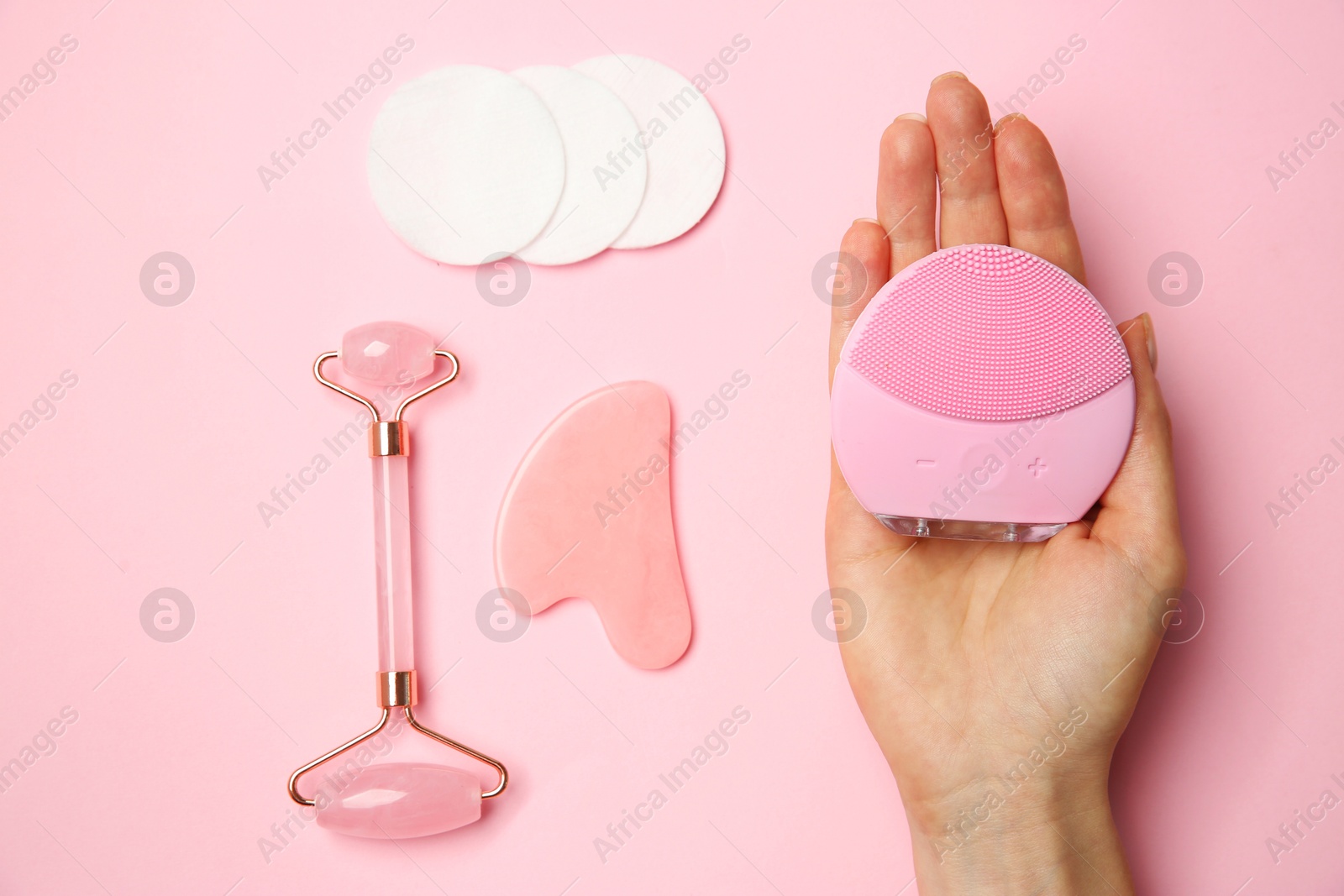 Photo of Woman holding facial cleansing brush near other skin care products on pink background, top view