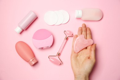 Photo of Woman holding gua sha tool near other skin care products on pink background, top view