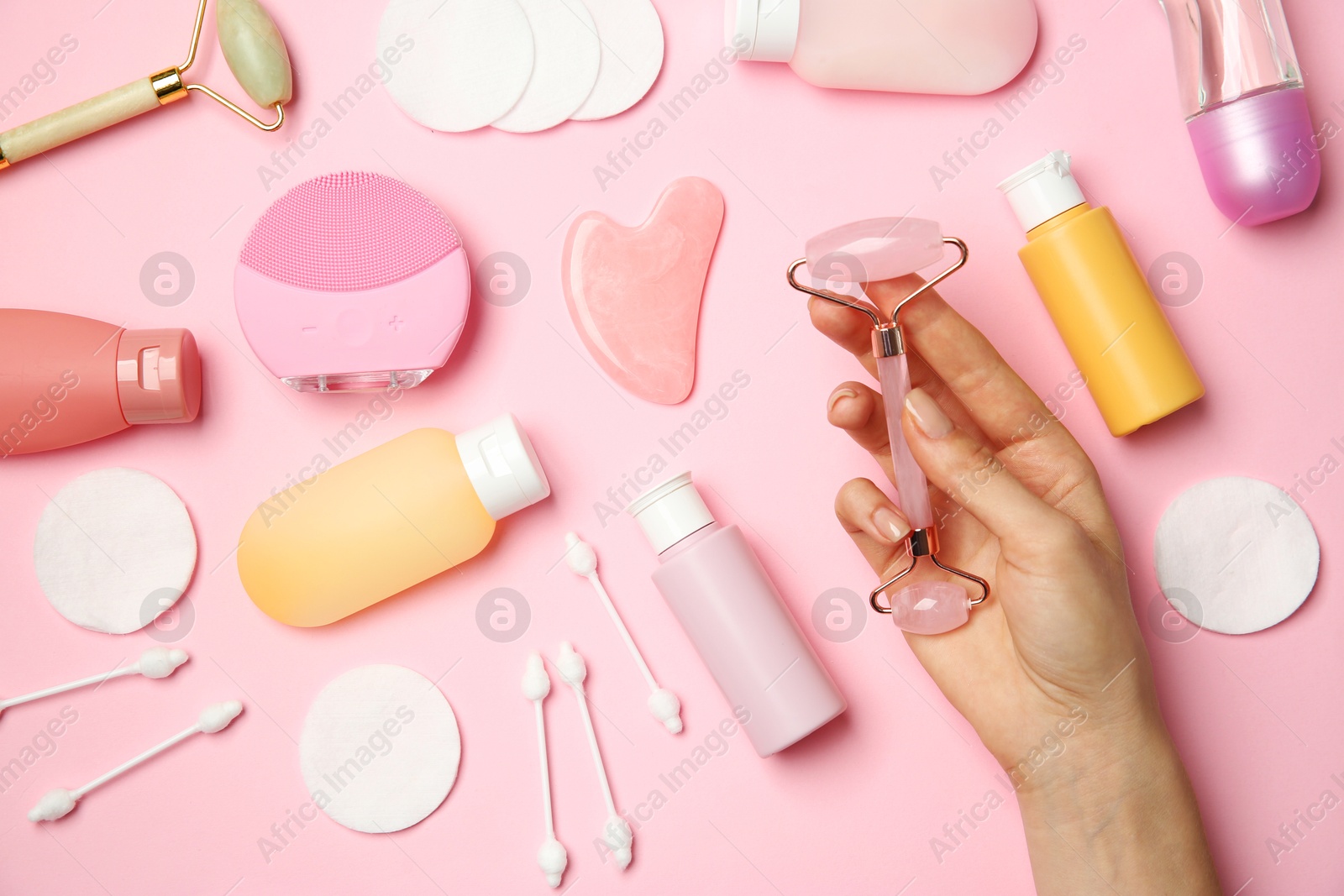 Photo of Woman holding facial roller near other skin care products on pink background, top view