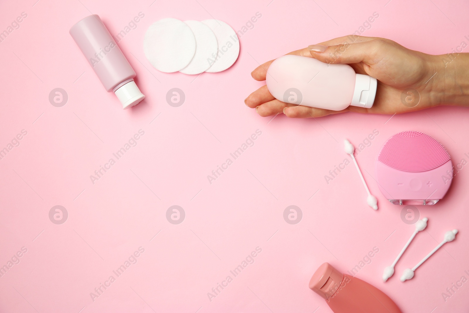 Photo of Woman holding cream near other skin care products on pink background, top view