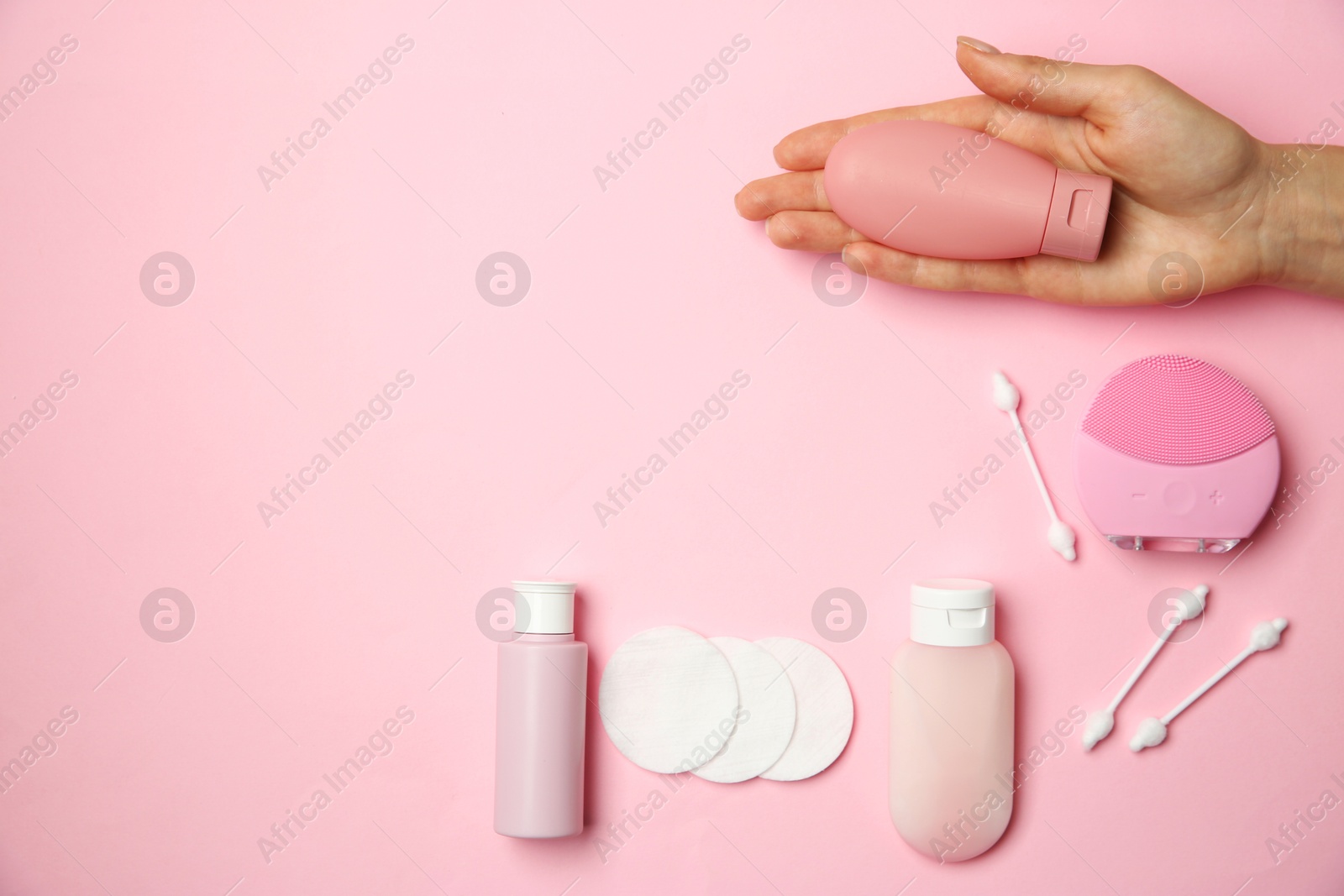 Photo of Woman holding cream near other skin care products on pink background, top view