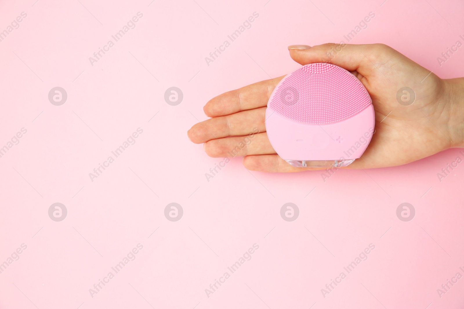 Photo of Woman holding facial cleansing brush on pink background, top view. Space for text