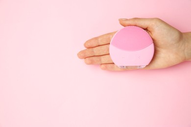 Photo of Woman holding facial cleansing brush on pink background, top view. Space for text