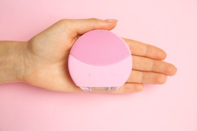 Photo of Woman holding facial cleansing brush on pink background, top view