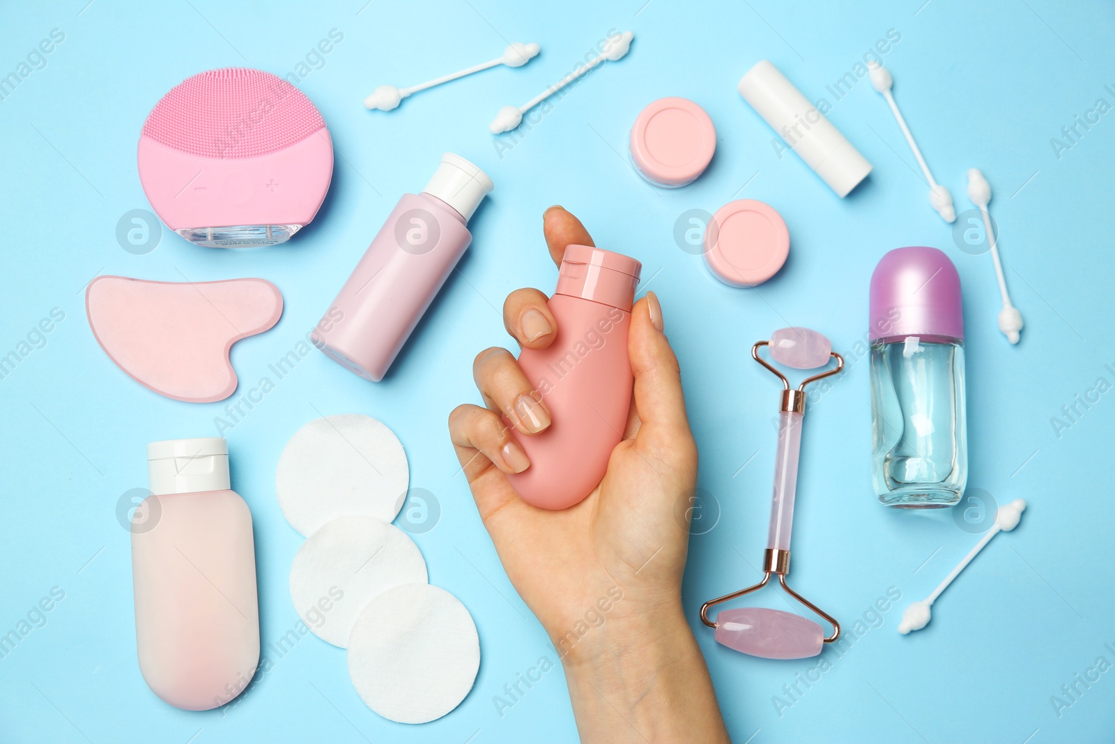 Photo of Woman holding lotion near other body care products on light blue background, top view