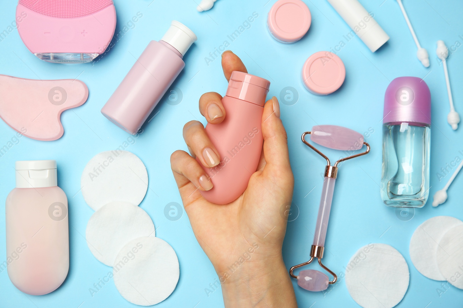 Photo of Woman holding lotion near other body care products on light blue background, top view