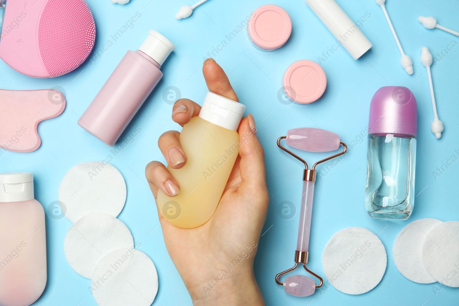 Photo of Woman holding lotion near other body care products on light blue background, top view