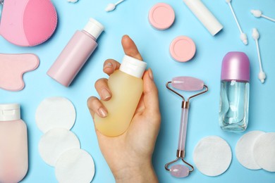 Photo of Woman holding lotion near other body care products on light blue background, top view