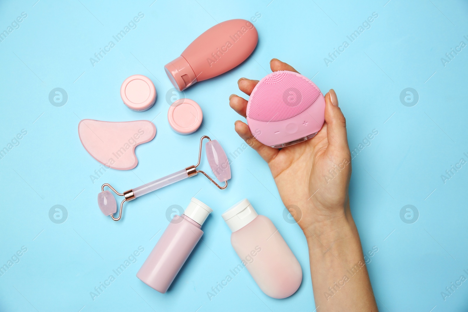 Photo of Woman holding facial cleansing brush near other skin care products on light blue background, top view