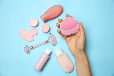 Photo of Woman holding facial cleansing brush near other skin care products on light blue background, top view