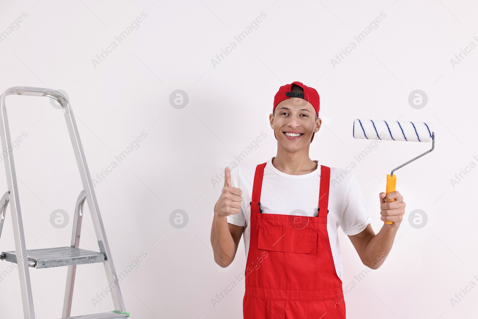 Photo of Smiling handyman with paint roller showing thumbs up indoors