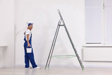 Photo of Happy handyman painting wall with roller near ladder indoors