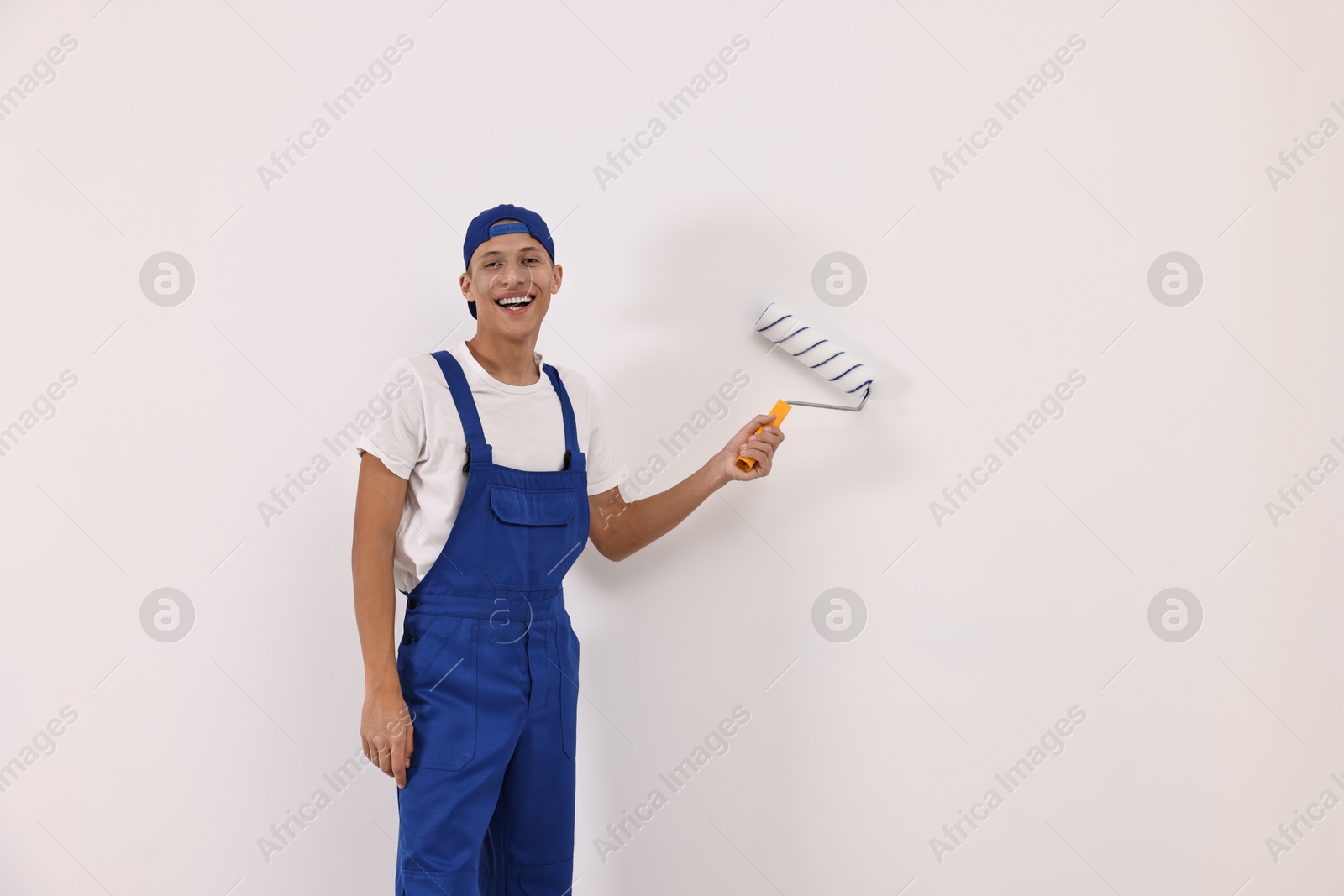 Photo of Smiling handyman painting wall with roller indoors. Space for text