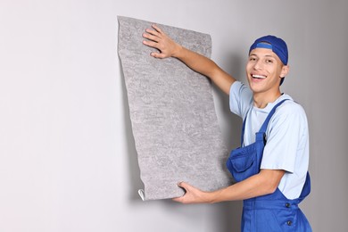 Photo of Smiling handyman hanging grey wallpaper on wall indoors