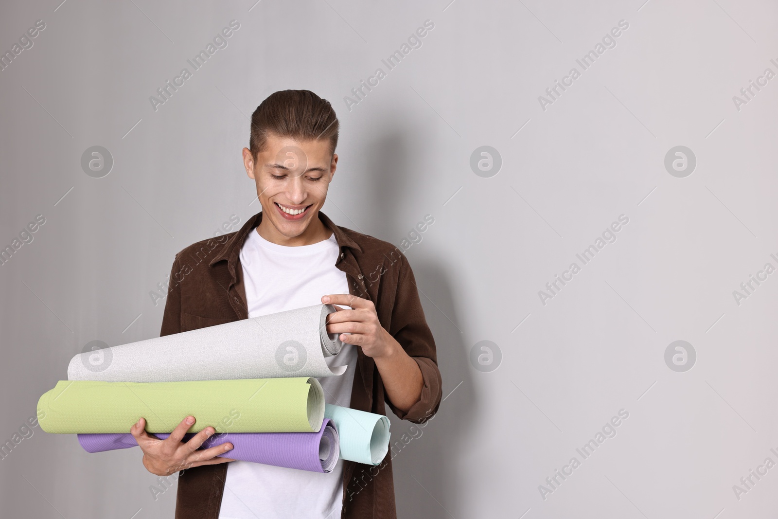 Photo of Smiling handyman with rolls of wallpaper indoors. Space for text