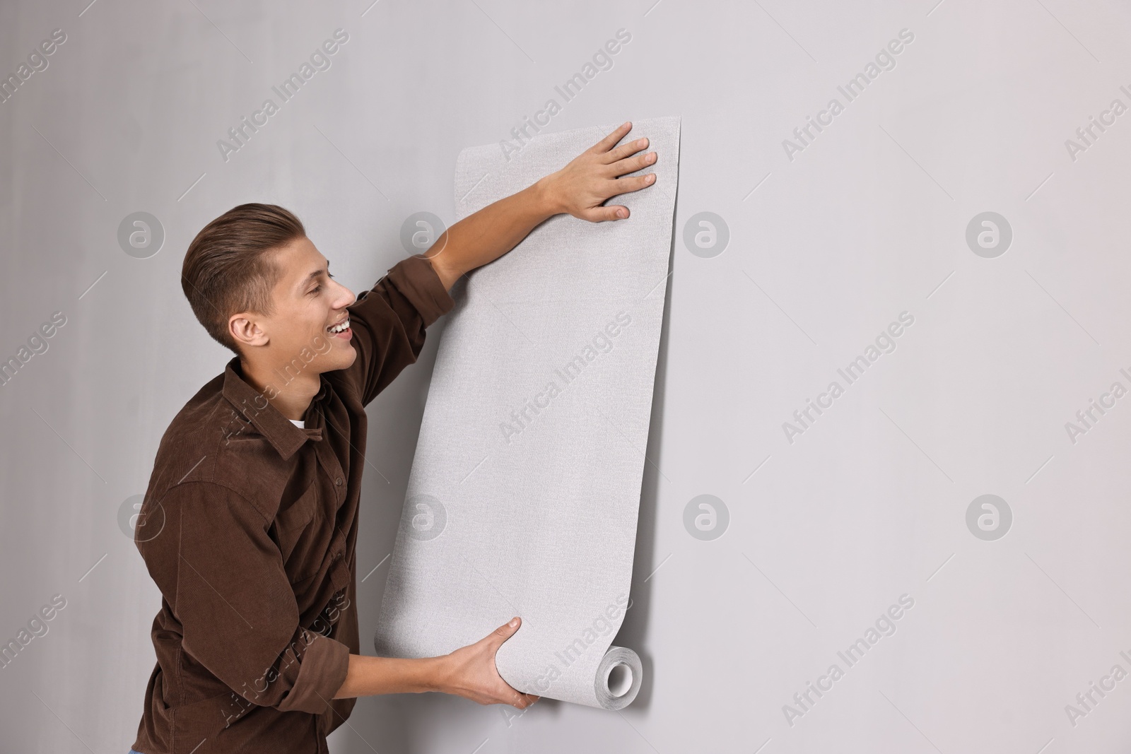 Photo of Smiling handyman hanging wallpaper indoors. Space for text