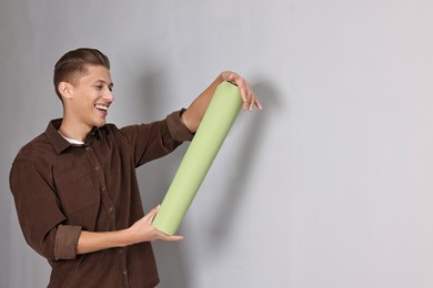 Photo of Smiling handyman with roll of wallpaper indoors. Space for text