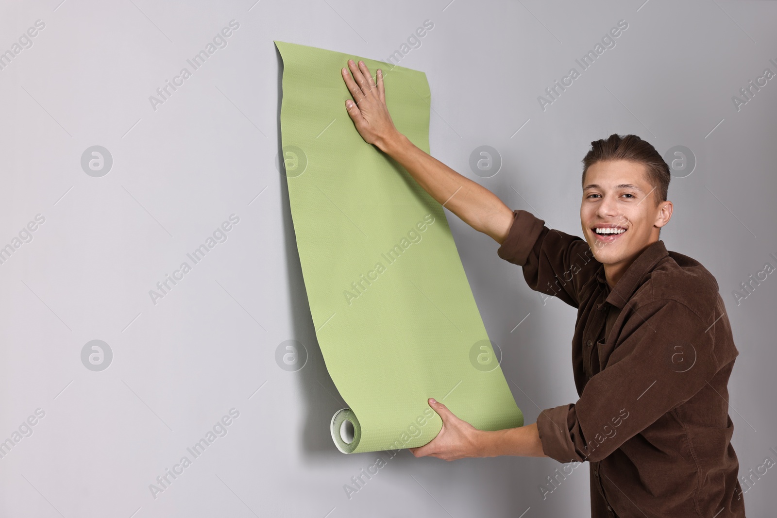 Photo of Smiling handyman hanging green wallpaper indoors. Space for text