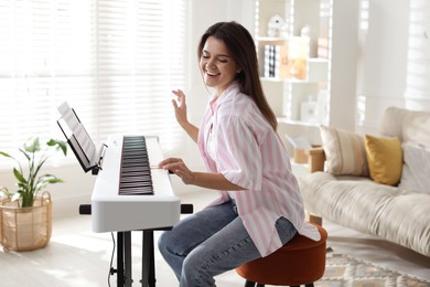 Photo of Smiling woman playing synthesizer at home. Electronic musical instrument