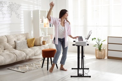 Photo of Smiling woman playing synthesizer and dancing at home