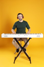 Photo of Smiling man in headphones playing synthesizer on orange background