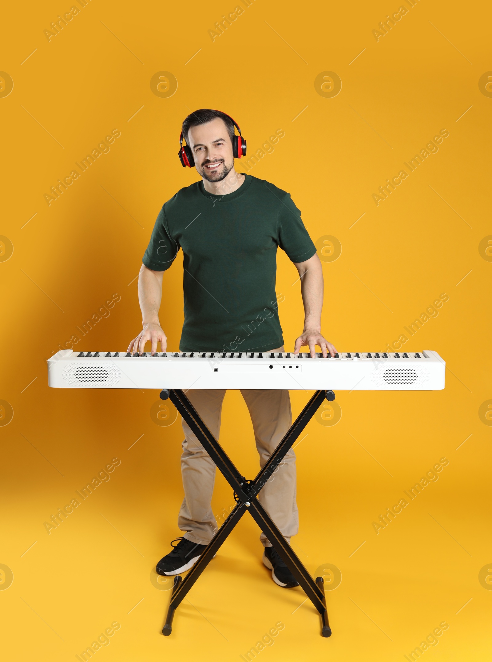 Photo of Smiling man in headphones playing synthesizer on orange background