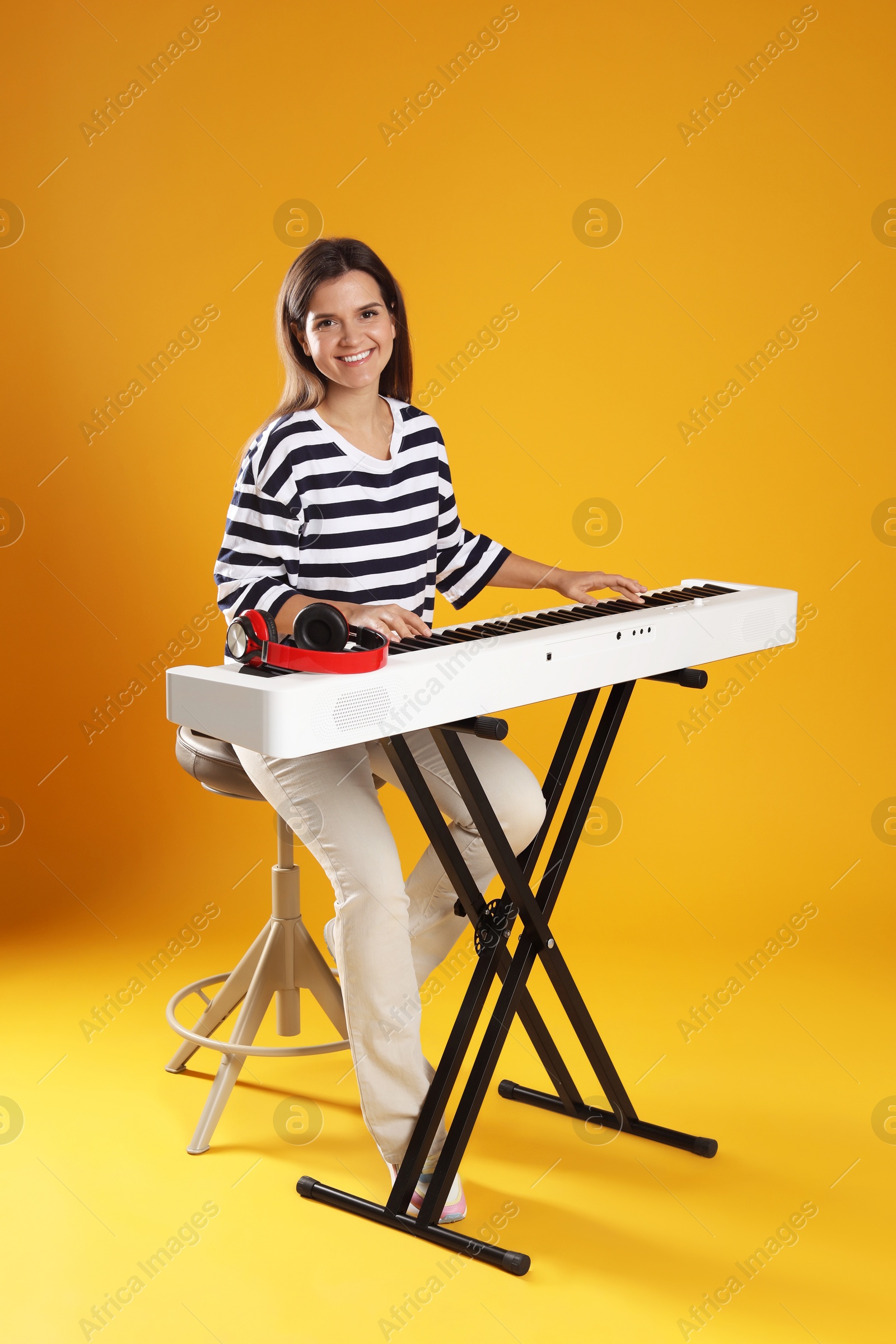 Photo of Smiling woman playing synthesizer on orange background