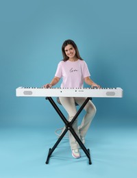 Photo of Smiling woman playing synthesizer on light blue background