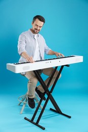 Photo of Smiling man playing synthesizer on light blue background