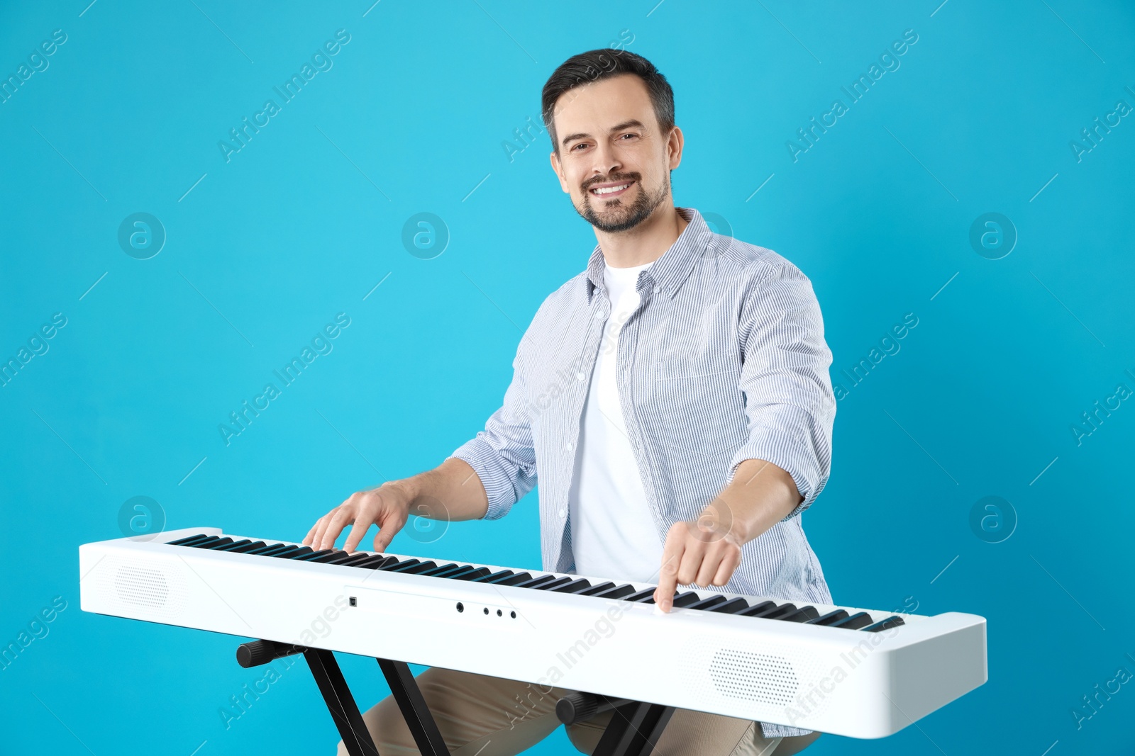 Photo of Smiling man playing synthesizer on light blue background