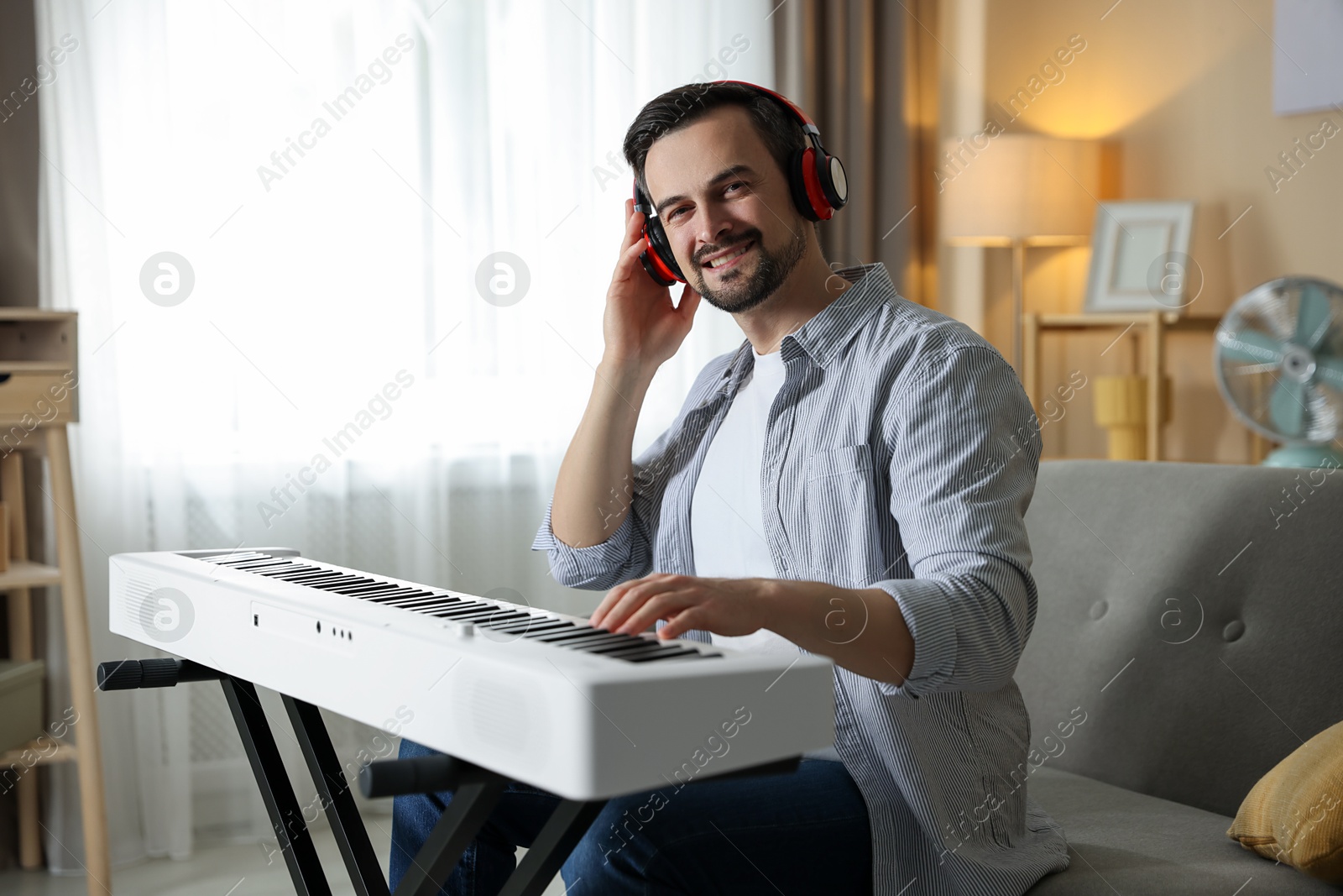 Photo of Smiling man in headphones playing synthesizer at home