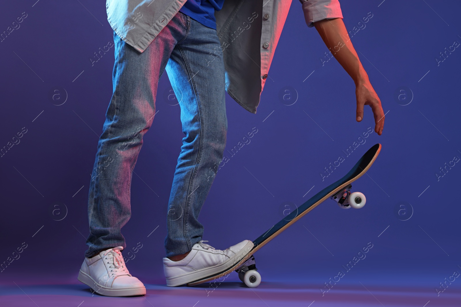 Photo of Man with skateboard in color lights against blue background, closeup