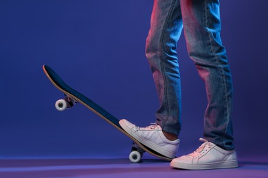 Photo of Man with skateboard in color lights against blue background, closeup