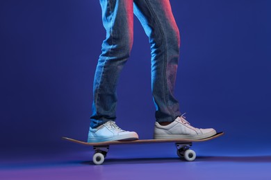 Photo of Man riding skateboard in color lights against blue background, closeup