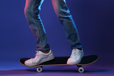 Photo of Man riding skateboard in color lights against blue background, closeup