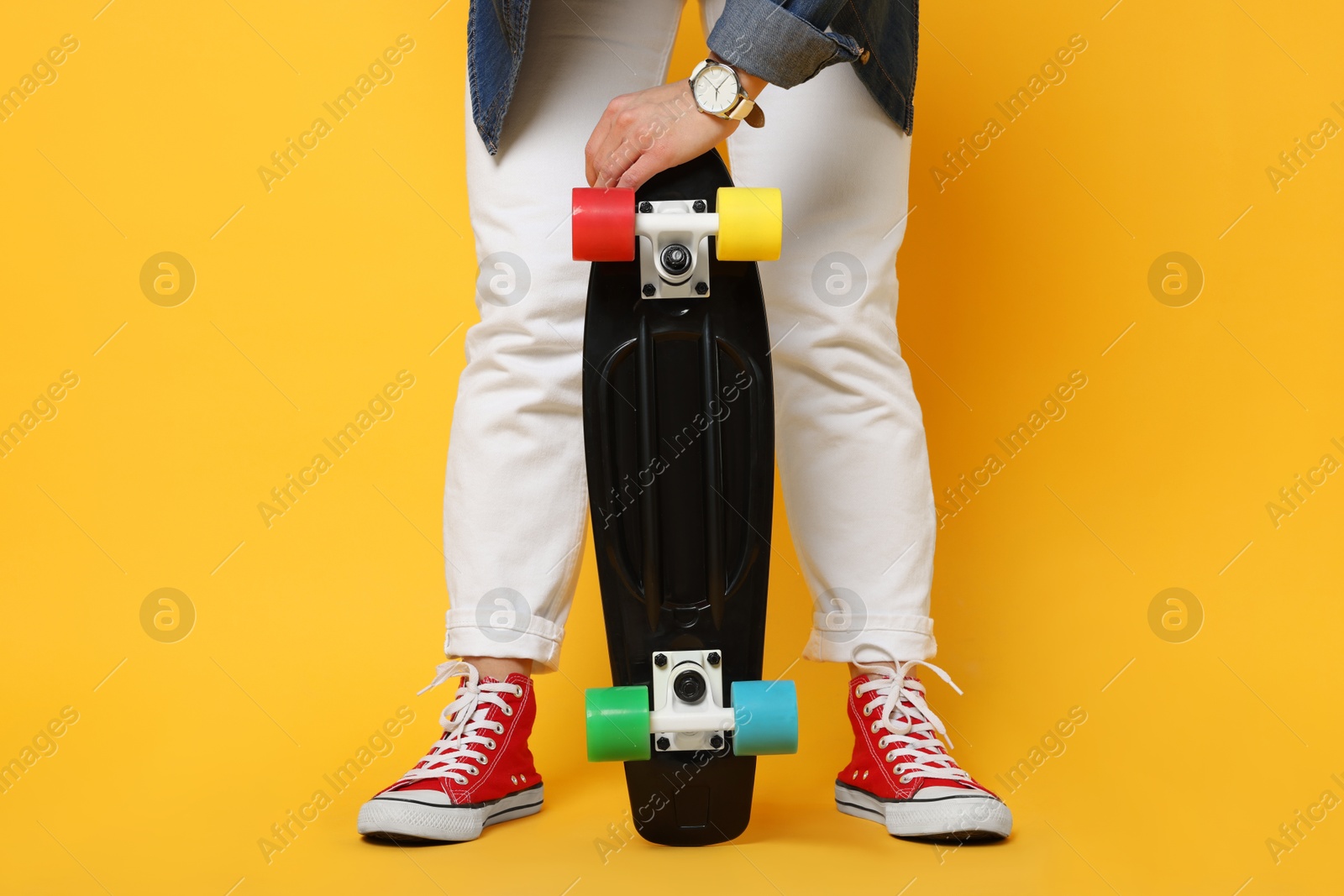 Photo of Woman with penny board on orange background, closeup