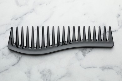 Photo of One black plastic comb on white marble table, top view