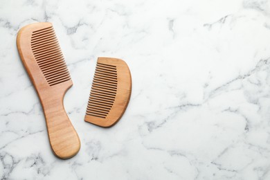 Different wooden hair combs on white marble table, top view. Space for text