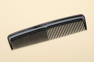 Photo of One black plastic comb on beige background, top view